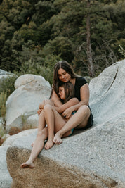 Beautiful mother and daughter sitting closely on a rock in a forested area