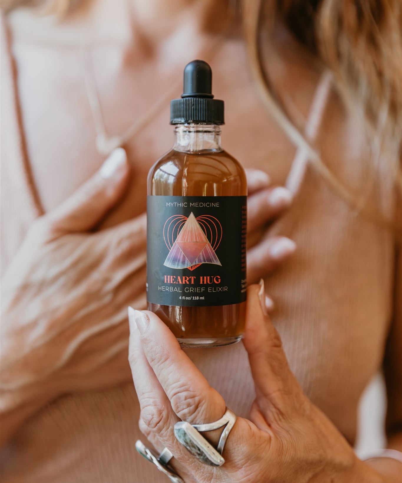 Person holding a bottle of 'Heart  Hug Herbal'  Mythic Medicine tincture with a blurred background