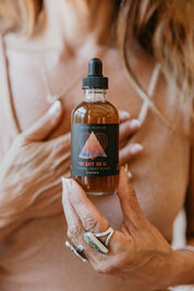 Person holding a bottle of 'Heart  Hug Herbal'  Mythic Medicine tincture with a blurred background