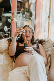 Pregnant woman sitting on a couch holding a bottle of Mythic Medicine in a cozy indoor setting