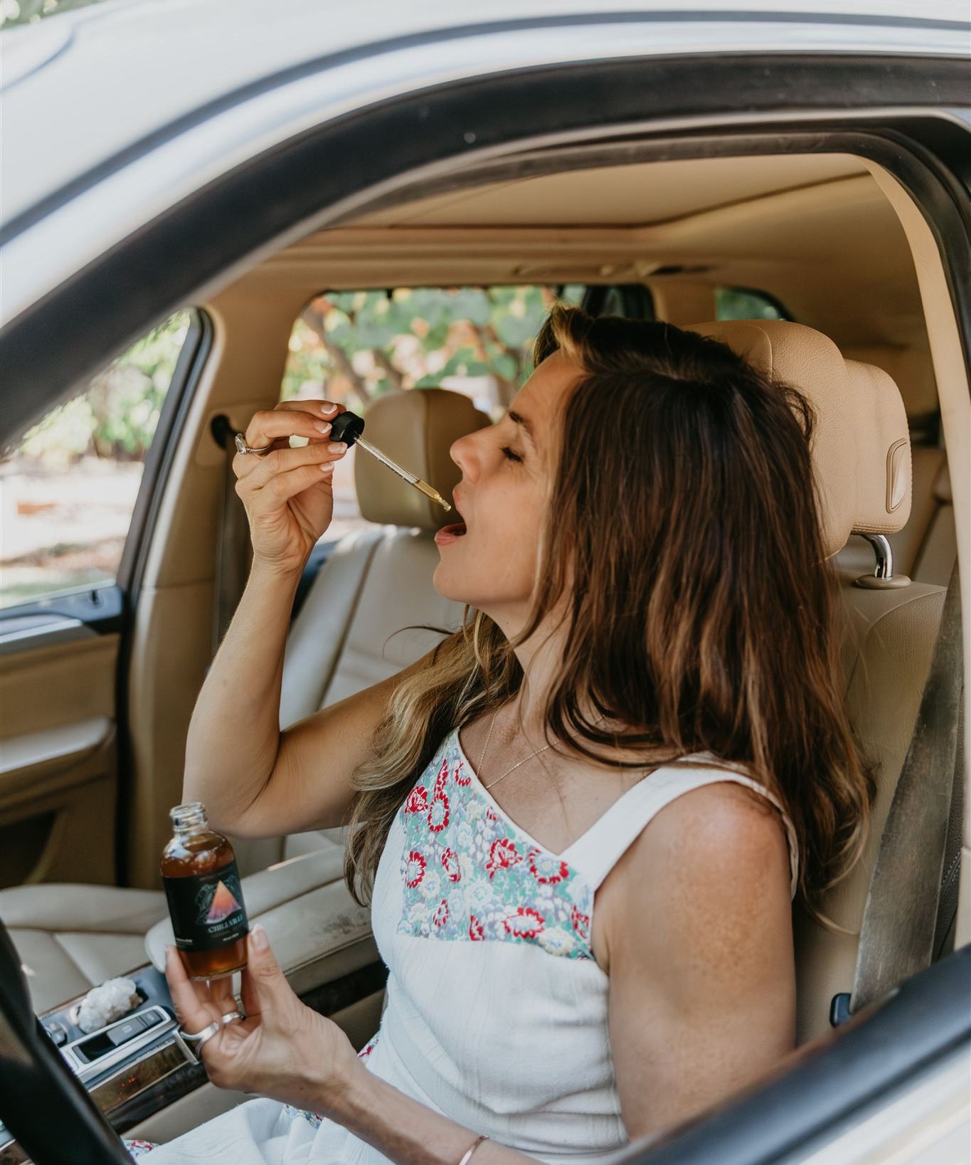 Woman sitting in a car, drinking from tincture bottle of Mythic Medicine