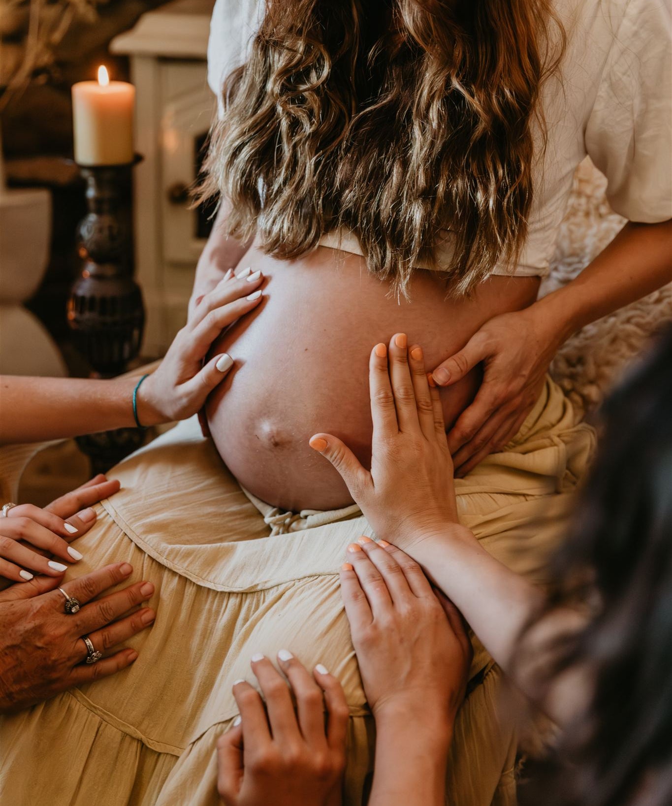 Pregnant woman with hands on her belly, surrounded by people in a warm setting.