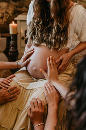 Pregnant woman with hands on her belly, surrounded by people in a warm setting.