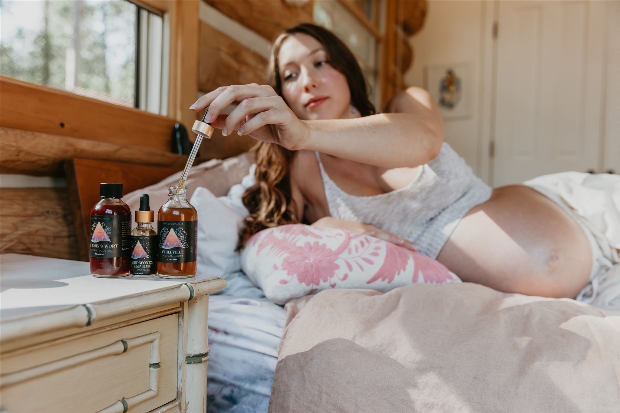 Woman lying on a bed with bottles of Mythic Medicine on a nightstand.