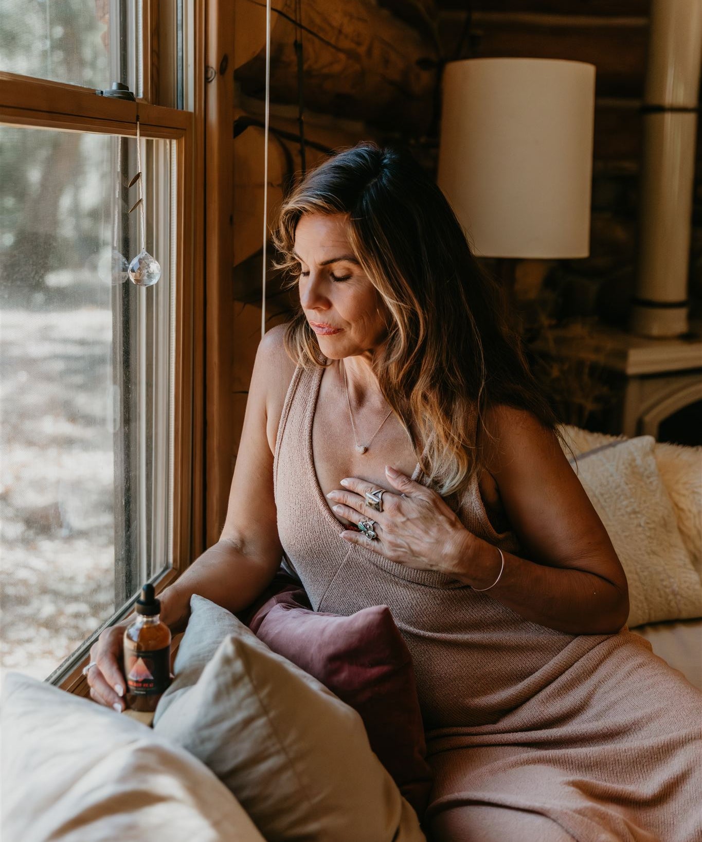 Woman sitting on a bed in a cozy log cabin room with large windows.