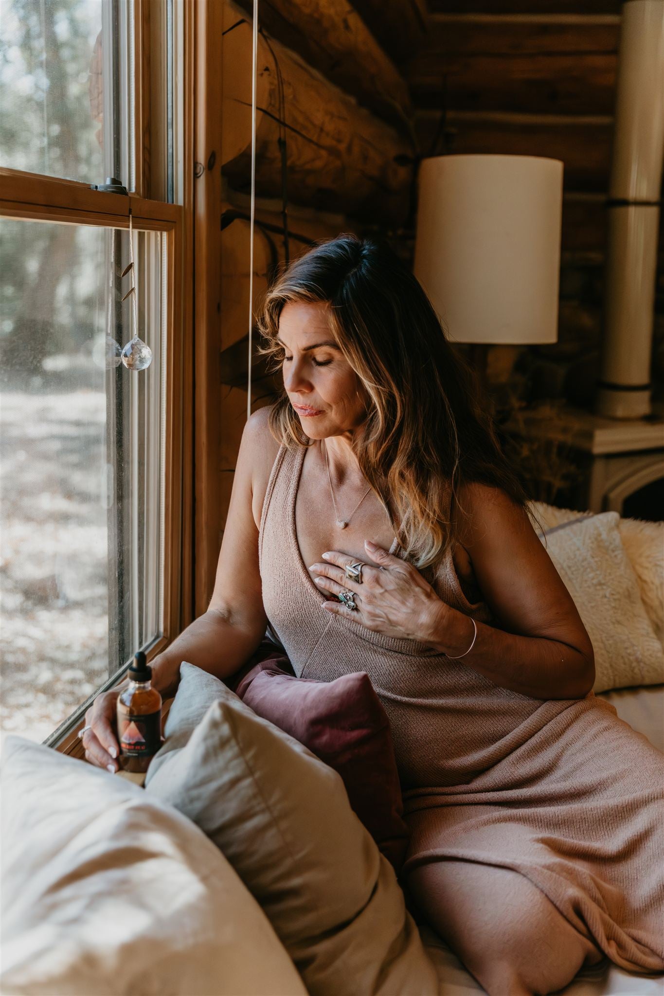 Woman sitting on a bed in a cozy log cabin room with large windows.
