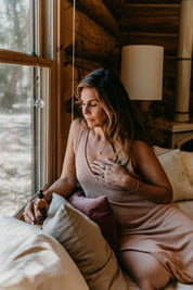 Woman sitting on a bed in a cozy log cabin room with large windows.