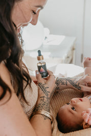 Woman holding a bottle of Mythic medicine Kinship essence next to a baby
