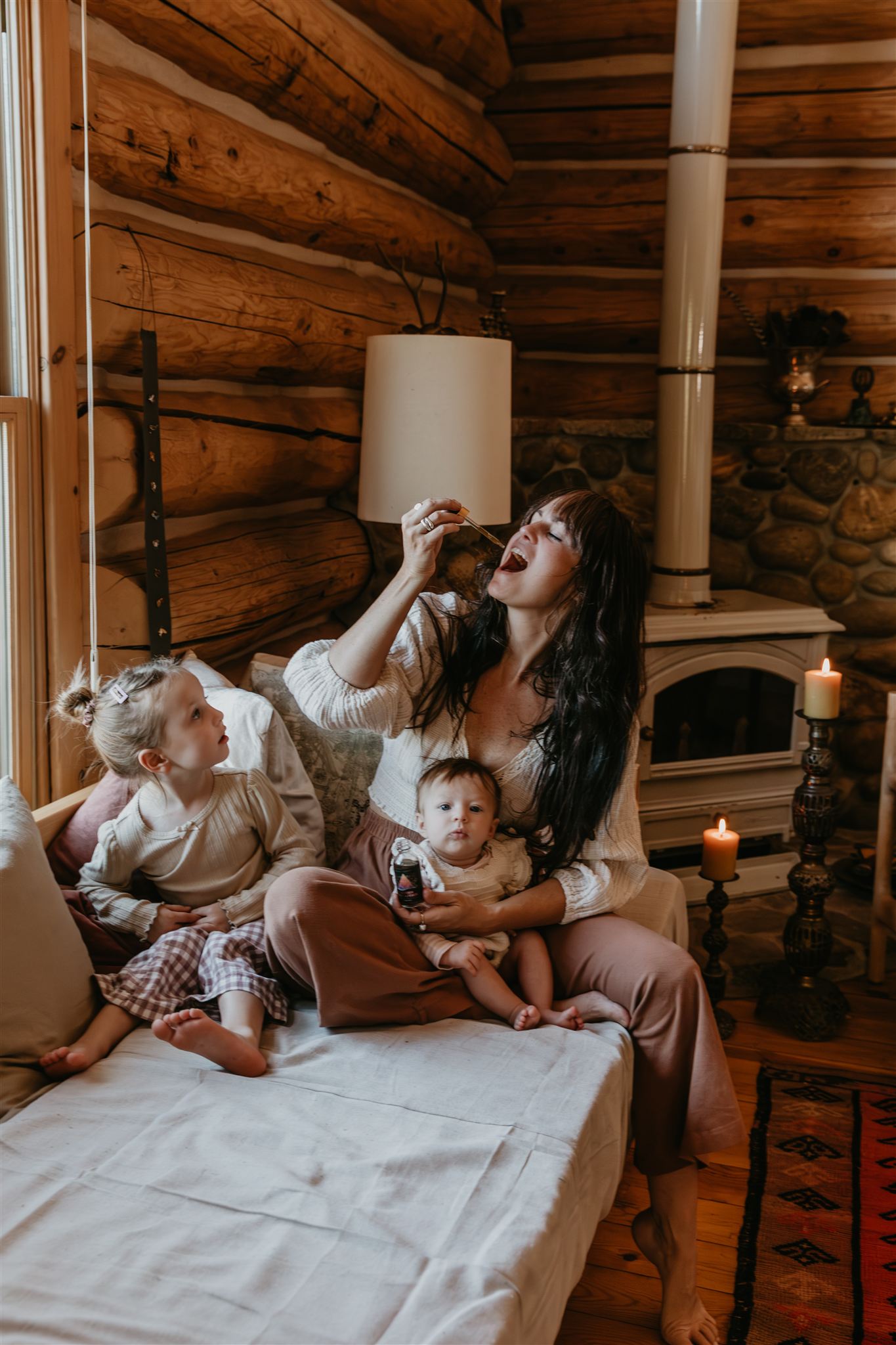 Woman and two children sitting on a bed in a cozy log cabin.