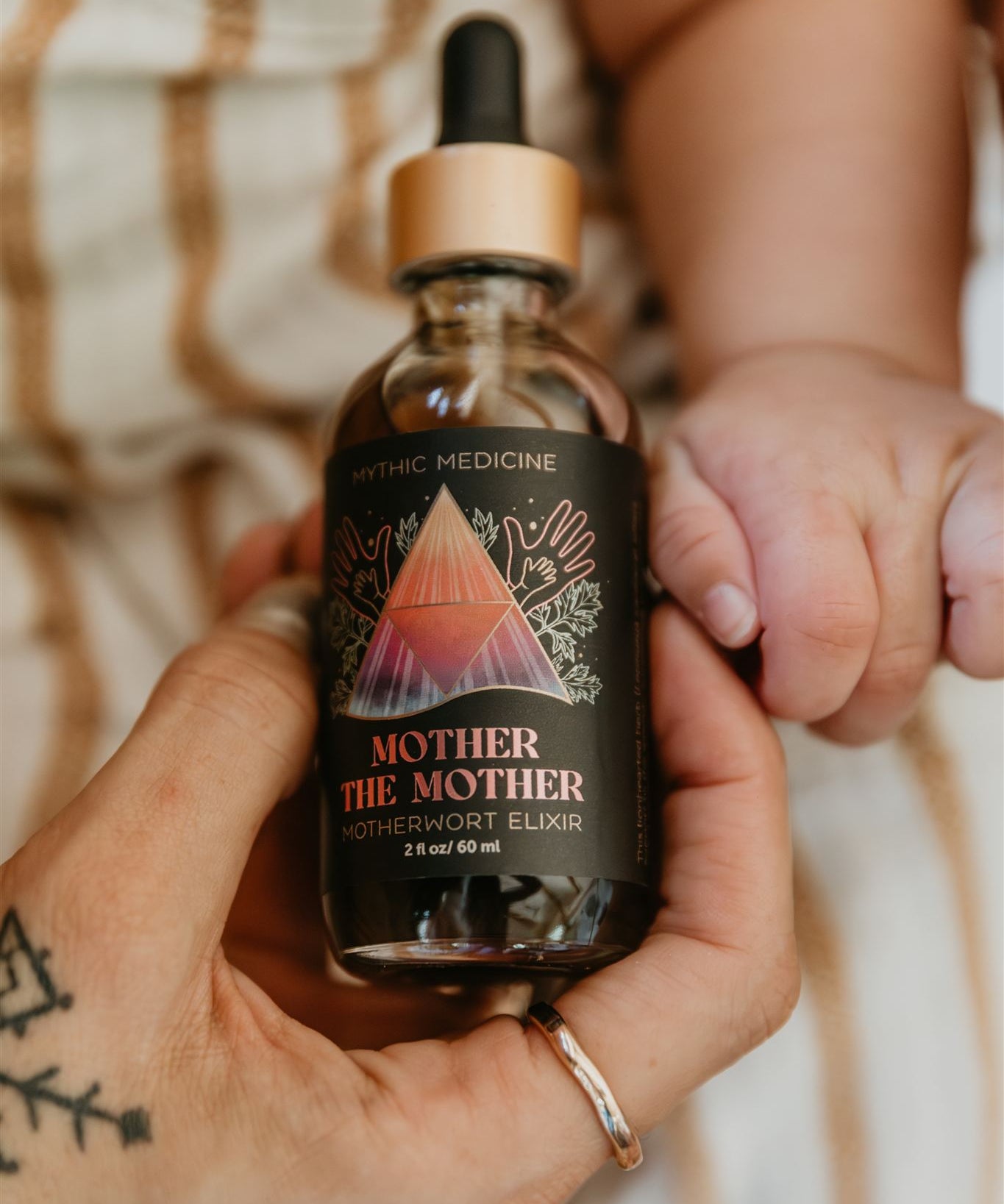 Bottle of 'Mother the Mother' elixir held by a hand with a blurred background