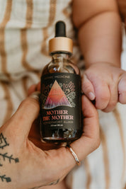 Bottle of 'Mother the Mother' elixir held by a hand with a blurred background