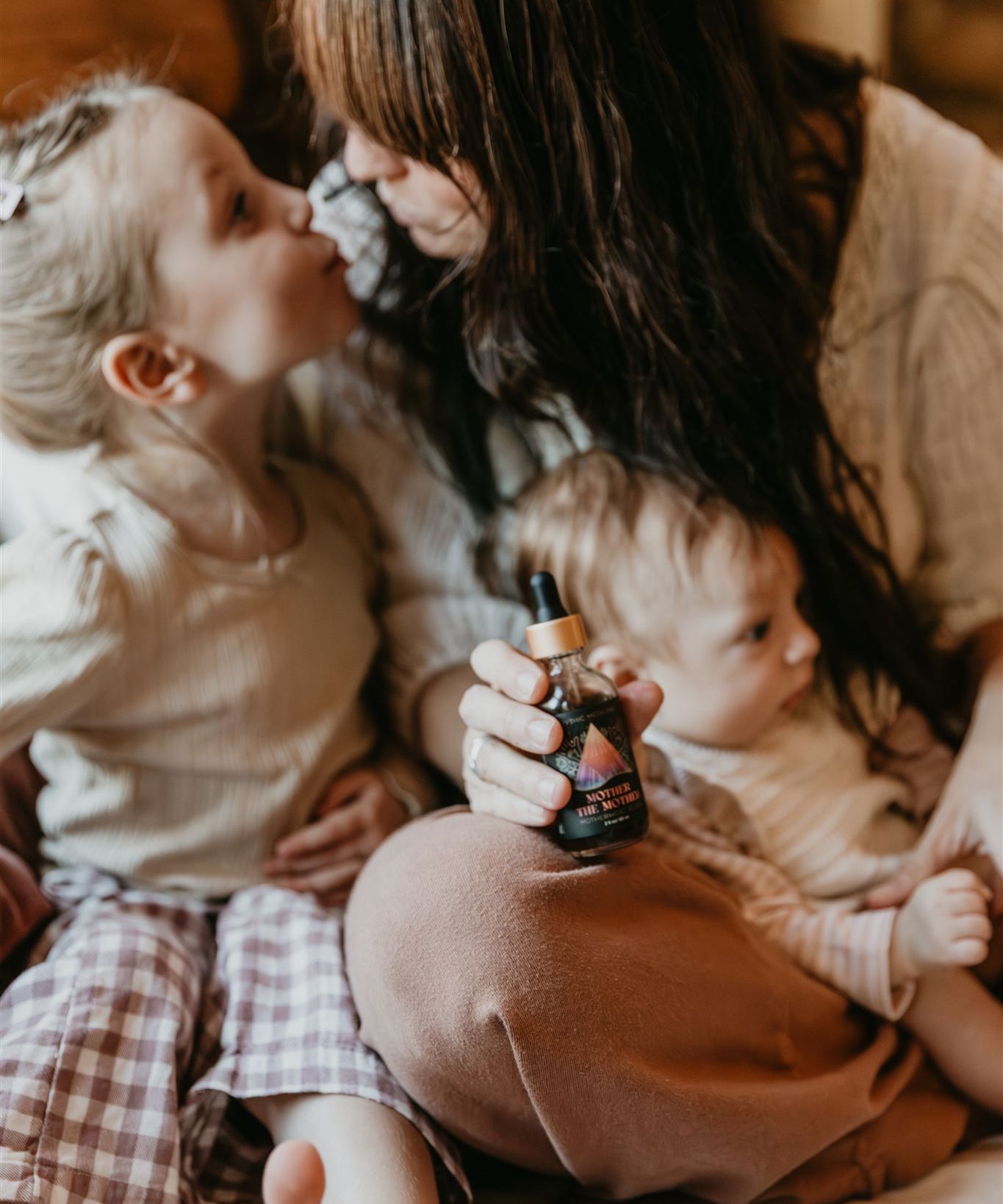 Woman holding a baby and a child, with a bottle of Mythic medicine in the woman's hand, in a warm indoor setting.