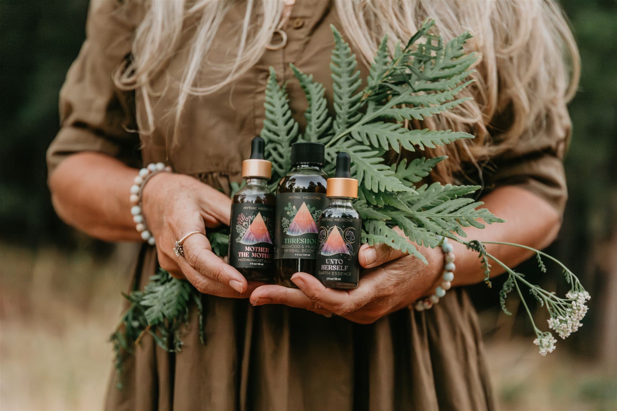 Person holding three bottles of Mythic Medicine with a natural setting