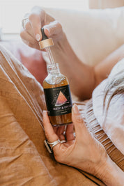 Person holding a bottle of Mythic Medicine 'Sleep & Dream' essential oil blend on a bed.