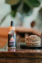 Bottle of 'What is Within You' earth tonic with a dropper on a wooden surface.