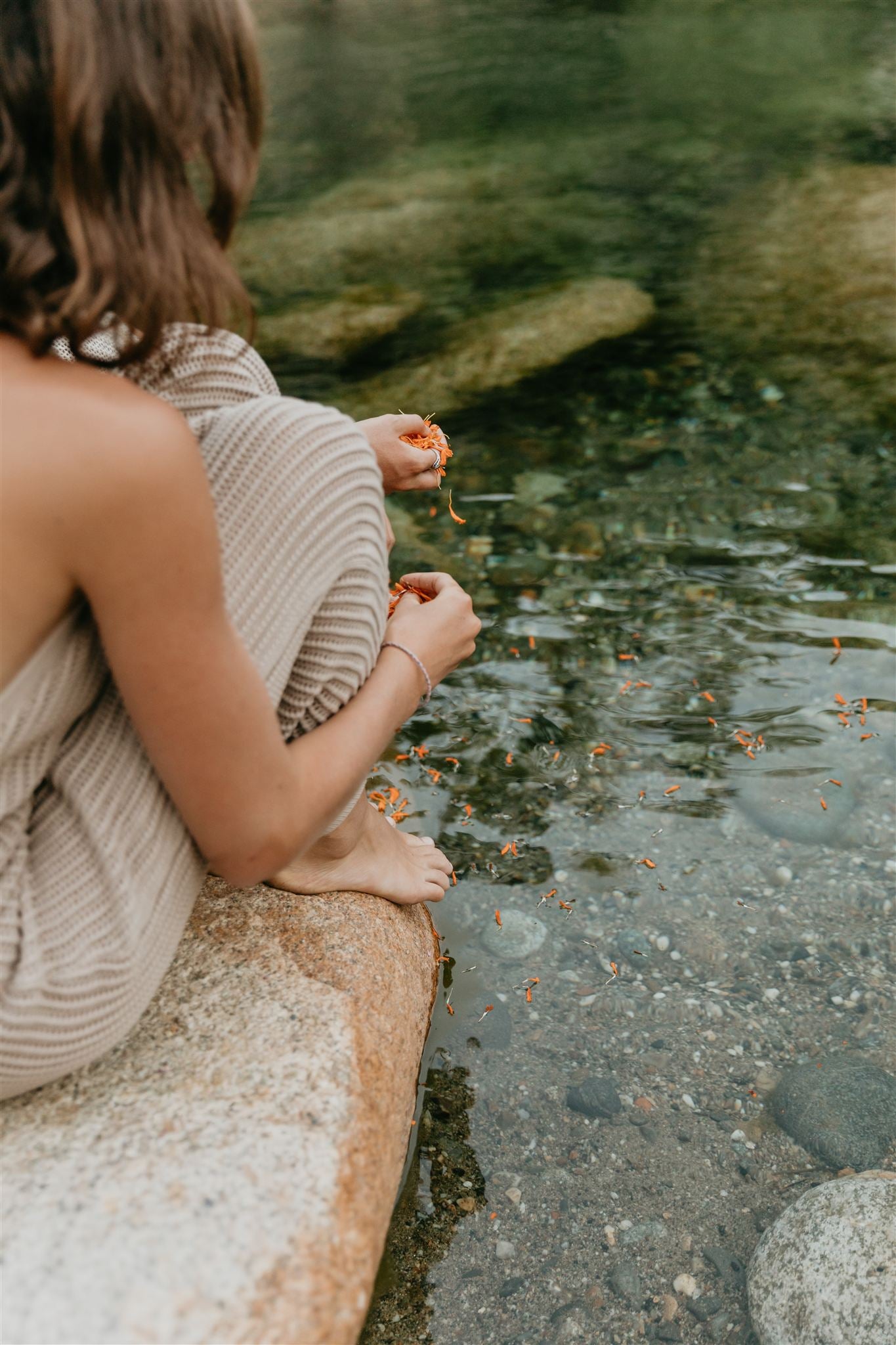 Person sitting by a stream, looking at the water