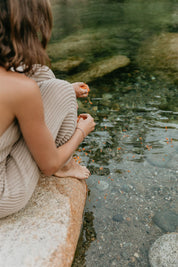 Person sitting by a stream, looking at the water