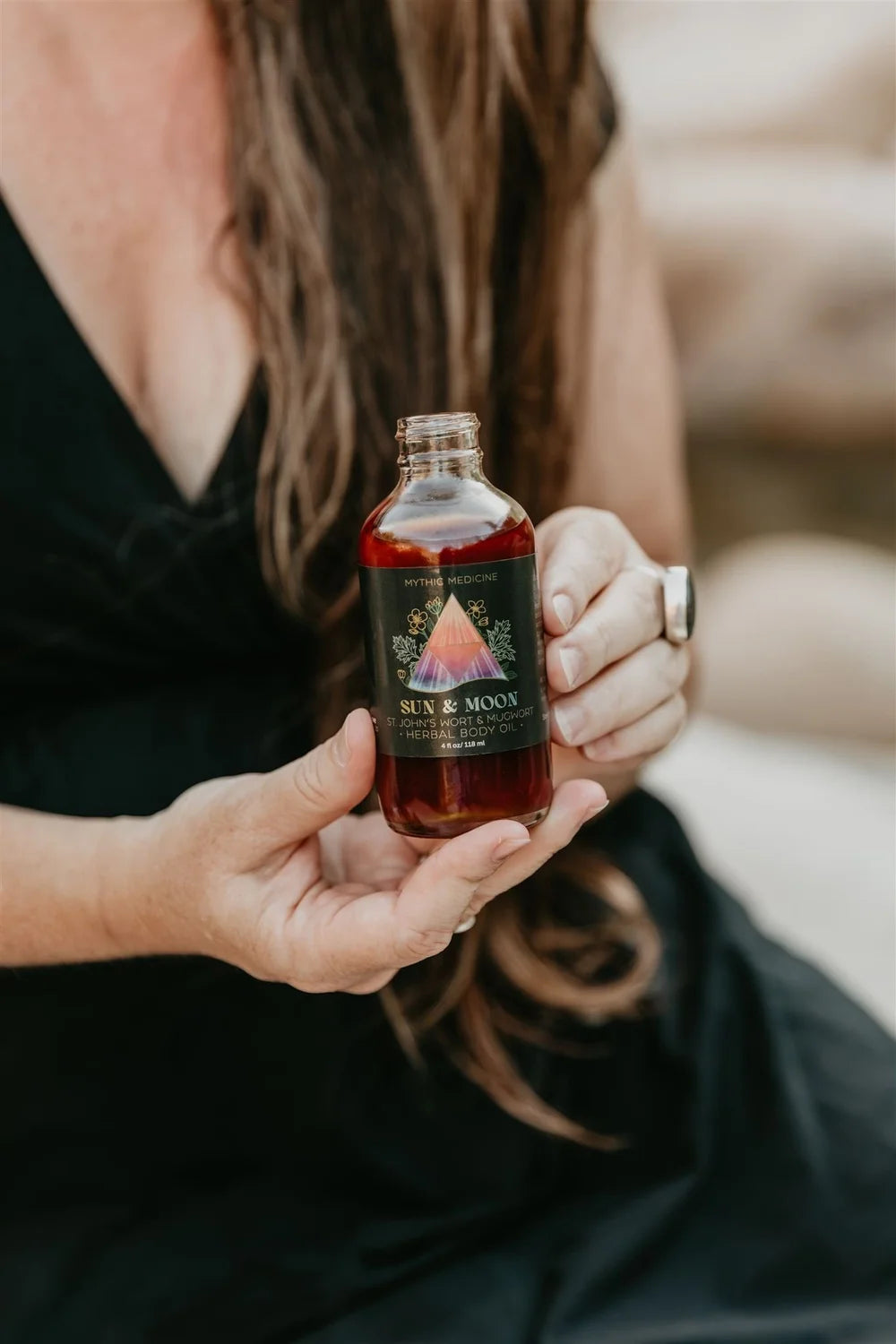Woman with long hair holding a bottle of Sun & Moon Mythic Medicine moonshine with a blurred background