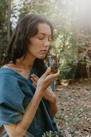 Woman holding a bottle of Mythic Medicine in a forest setting