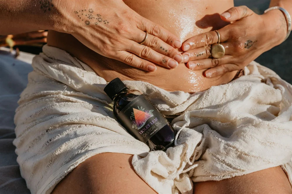 Person applying Violet Leaf Oil to their belly with a tattooed hands visible.