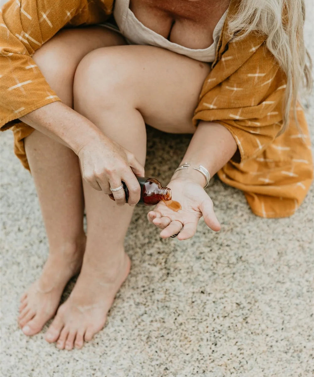 Woman applying St Johns Wort to her hand on a sandy surface