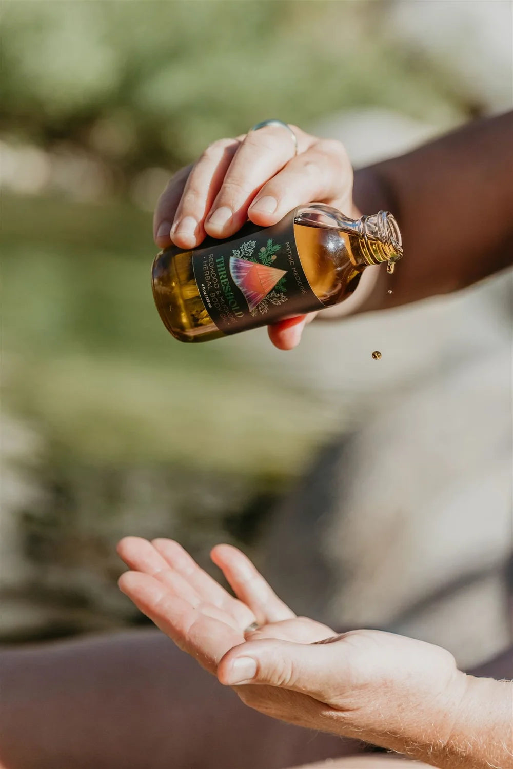 Hand pouring oil from a bottle onto another hand with a blurred natural background