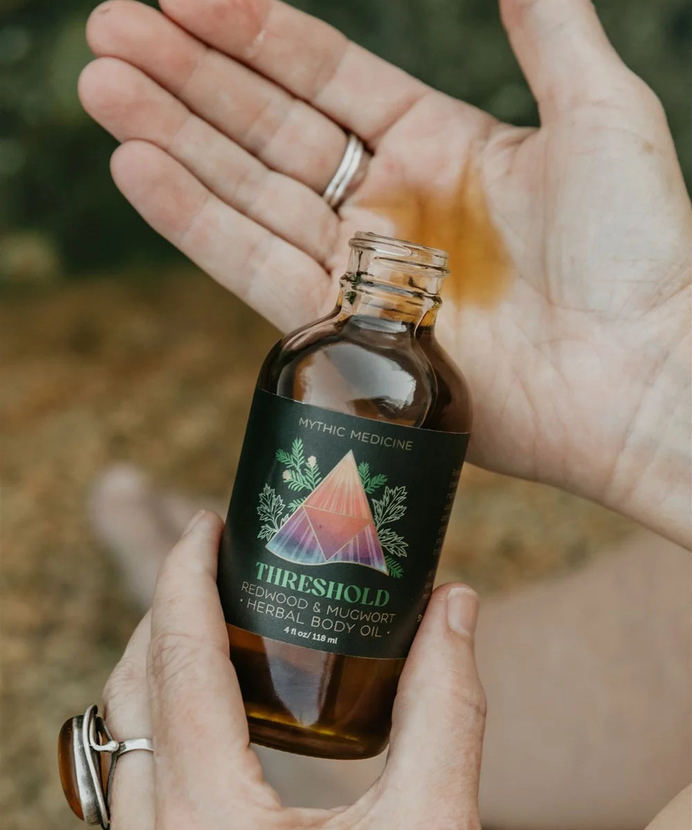 Hand holding a bottle of 'Threshold' body oil with a blurred natural background
