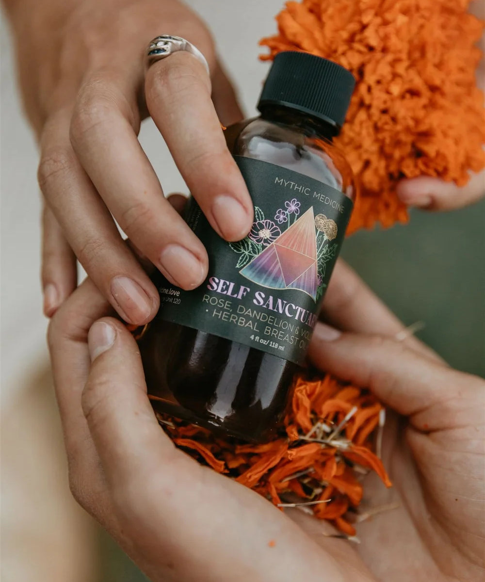 Bottle of 'Self Sanctify' with dried herbs held by hands against an orange textured background